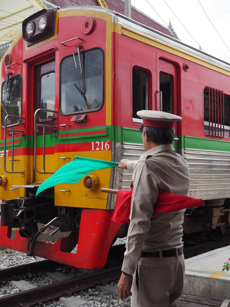 Train arriving at Ban Laem Railway Station, with conductor waving a flag