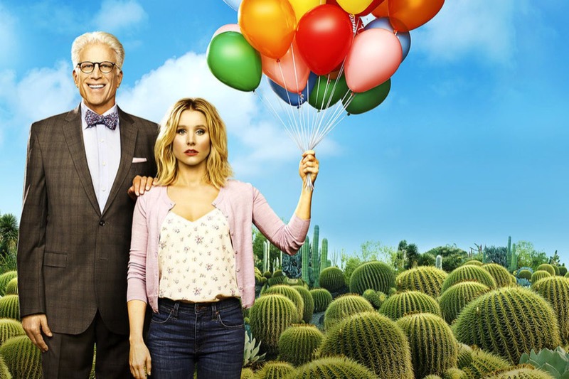 Poster for The Good Place: a tall man in a suit and an unhappy woman holding a bunch of colourful balloons stand in a field of cactus