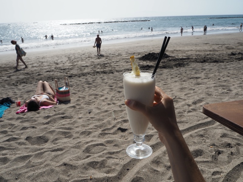 Hand holding up a cocktail on a sandy beach