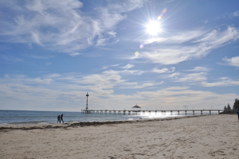 Beach in Adelaide, with sunshine, blue skies, white sand and a jetty visible in the distance