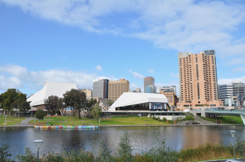 Adelaide skyline in the daytime, with the River Torrens in the foreground and the Entertainment Centre and city buildings in the background. Blue skies.